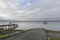 a dock with boats is empty and the water near it is very calm, with a few boats on the water