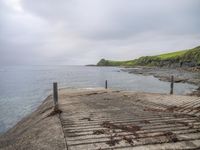 a dock with a railing overlooking a beach and a cliff in the distance and a green hillside in the distance