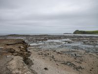 a small rocky beach and some sand water and grass with a lighthouse in the distance