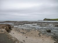 a small rocky beach and some sand water and grass with a lighthouse in the distance