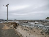 an empty beach with lots of water and some rocks, and a streetlight and walkway