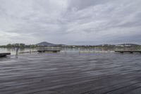 a wooden dock with benches under the water on the edge of a lake area with mountains and buildings on a cloudy day