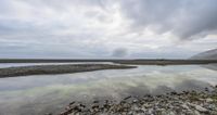 rocks and gravel near a shallow lake and mountains under cloudy skies in the scottish countryside