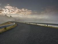 a curving road with a fog covered sky in the background and trees on the edge