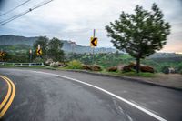 the back side of a car driving along the road near mountains and trees in the distance