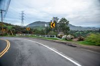 the back side of a car driving along the road near mountains and trees in the distance