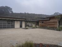 a large home with garage doors is located in the hillside area of the property with rocks and grasses