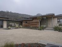 a large home with garage doors is located in the hillside area of the property with rocks and grasses