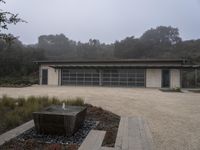 a very nice looking home with a nice water fountain in front of it with foggy trees behind it