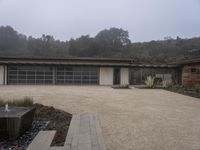 a very nice looking home with a nice water fountain in front of it with foggy trees behind it