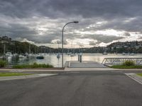 a view of a marina and dock from the street with boats on the water and dark clouds