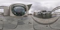 there is a circular mirror reflection of an office building and water fountain, which look like a fish eye