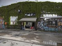 there are a lot of plants in this picture, with graffiti all over it and people walking along the street