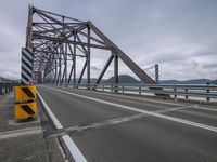 the bridge has yellow signs in front of it while traffic crosses over it on a cloudy day