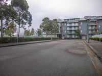 an empty road with two buildings on one side of it, trees on the other