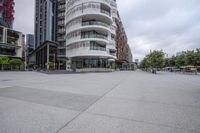 a group of people walking down a sidewalk near tall buildings in a city area with an odd structure