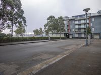 a street view with trees on either side of the road and blue buildings to the right