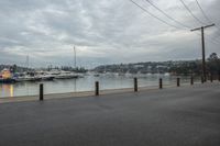 a harbor with several boats in the water and a man riding on the bike, with power lines over the water