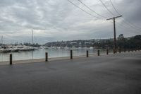 a harbor with several boats in the water and a man riding on the bike, with power lines over the water