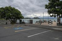 a street next to a parking space with benches and trees near it in front of the water