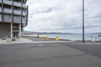 a empty parking lot next to the sea near some buildings and stairs on a beach