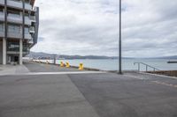 a empty parking lot next to the sea near some buildings and stairs on a beach