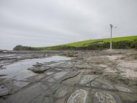 there are several stones on this beach and a wind turbine next to it with a hillside in the background