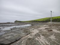 there are several stones on this beach and a wind turbine next to it with a hillside in the background