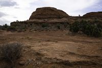 dirt covered landscape with a rocky cliff in the background and sparse brush on ground below