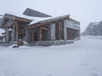 two cabins in a snowy setting near some buildings, with snow falling off the roof