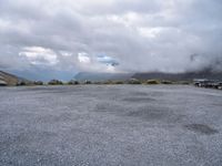 a parking lot on top of a mountain with clouds in the sky and two white cars parked near by