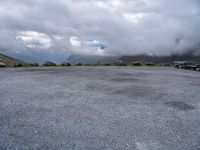 a parking lot on top of a mountain with clouds in the sky and two white cars parked near by