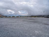 a parking lot on top of a mountain with clouds in the sky and two white cars parked near by