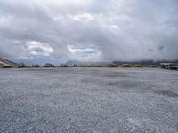 a parking lot on top of a mountain with clouds in the sky and two white cars parked near by