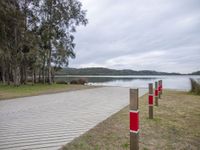 a boardwalk leading to a lake next to a forest with no people around it and red poles on either side