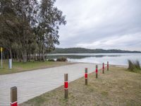 a boardwalk leading to a lake next to a forest with no people around it and red poles on either side