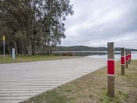 a boardwalk leading to a lake next to a forest with no people around it and red poles on either side