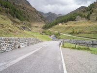 the road is going uphill in the mountains with a mountain pass by it and a stone bridge near the mountain