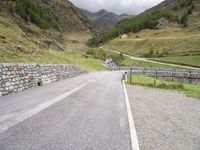 the road is going uphill in the mountains with a mountain pass by it and a stone bridge near the mountain