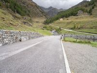 the road is going uphill in the mountains with a mountain pass by it and a stone bridge near the mountain