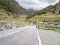 the road is going uphill in the mountains with a mountain pass by it and a stone bridge near the mountain