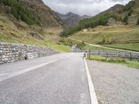 the road is going uphill in the mountains with a mountain pass by it and a stone bridge near the mountain