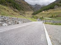 the road is going uphill in the mountains with a mountain pass by it and a stone bridge near the mountain