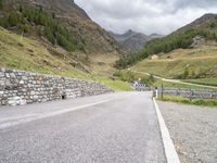 the road is going uphill in the mountains with a mountain pass by it and a stone bridge near the mountain