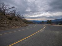 a mountain road with a lone sign on it and clouds above the hills in the background