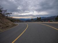 a mountain road with a lone sign on it and clouds above the hills in the background