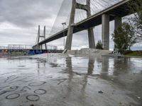 a large bridge in the background and graffiti on a concrete platform underneath it is covered in rain