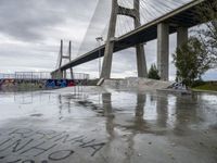 a large bridge in the background and graffiti on a concrete platform underneath it is covered in rain