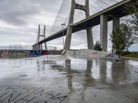 a large bridge in the background and graffiti on a concrete platform underneath it is covered in rain