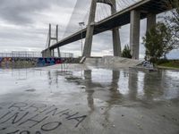 a large bridge in the background and graffiti on a concrete platform underneath it is covered in rain